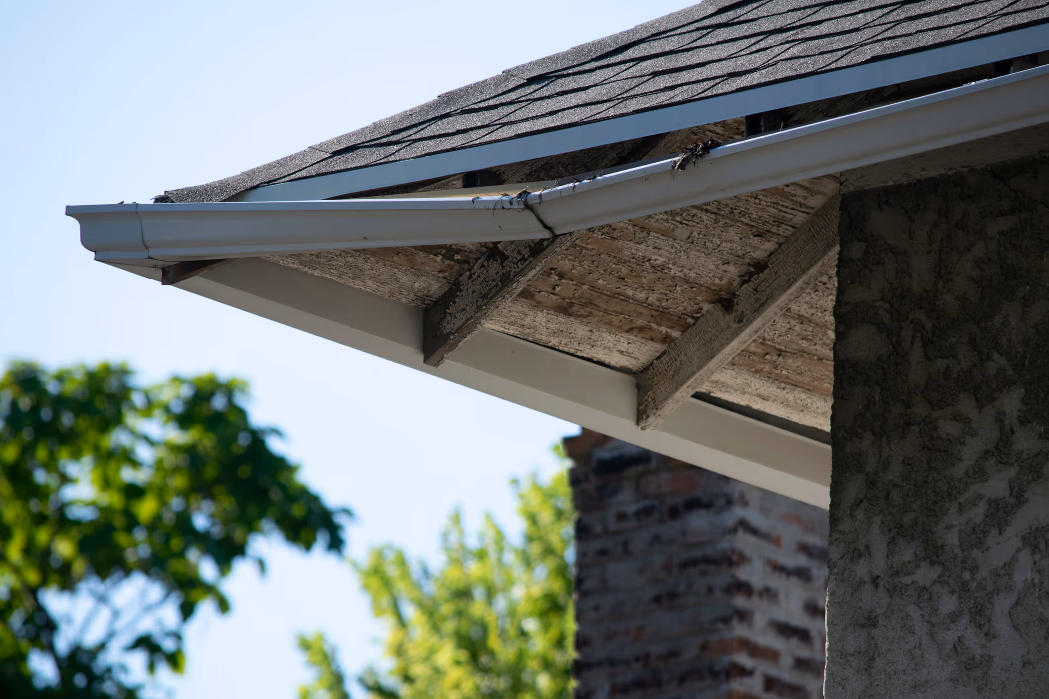 A close-up view of a white aluminum gutter along a residential roofline showing visible debris buildup and signs of wear near the fascia and soffit.